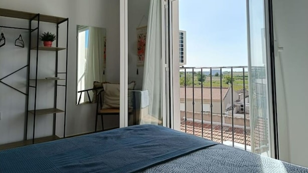 Un dormitorio con cama, armario, silla y balcón con vista a la ciudad.