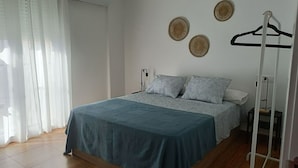 Un dormitorio con cama, mesita de noche, lámpara colgante y ventana con cortinas.