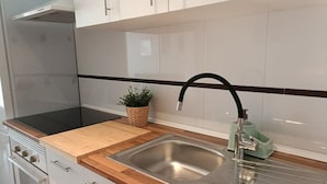Una cocina con armarios blancos, un lavamanos de acero inoxidable, encimera de madera y horno empotrado.