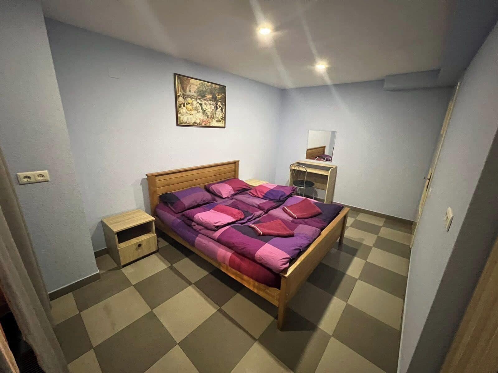 A bedroom with a wooden bed, a small bedside table, a dresser, and a mirror.