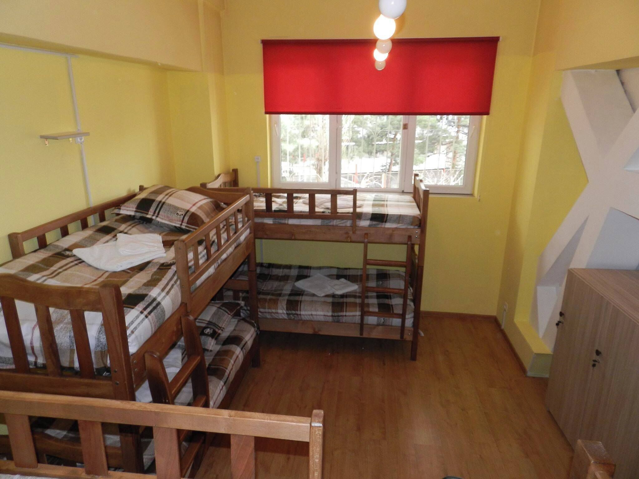 Une chambre de dortoir avec deux lits superposés, une fenêtre avec un store rouge et une armoire en bois.