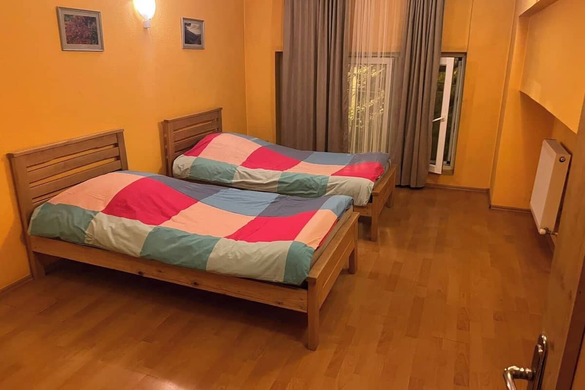 A room with two wooden beds, a window with curtains, and a radiator on the wall.