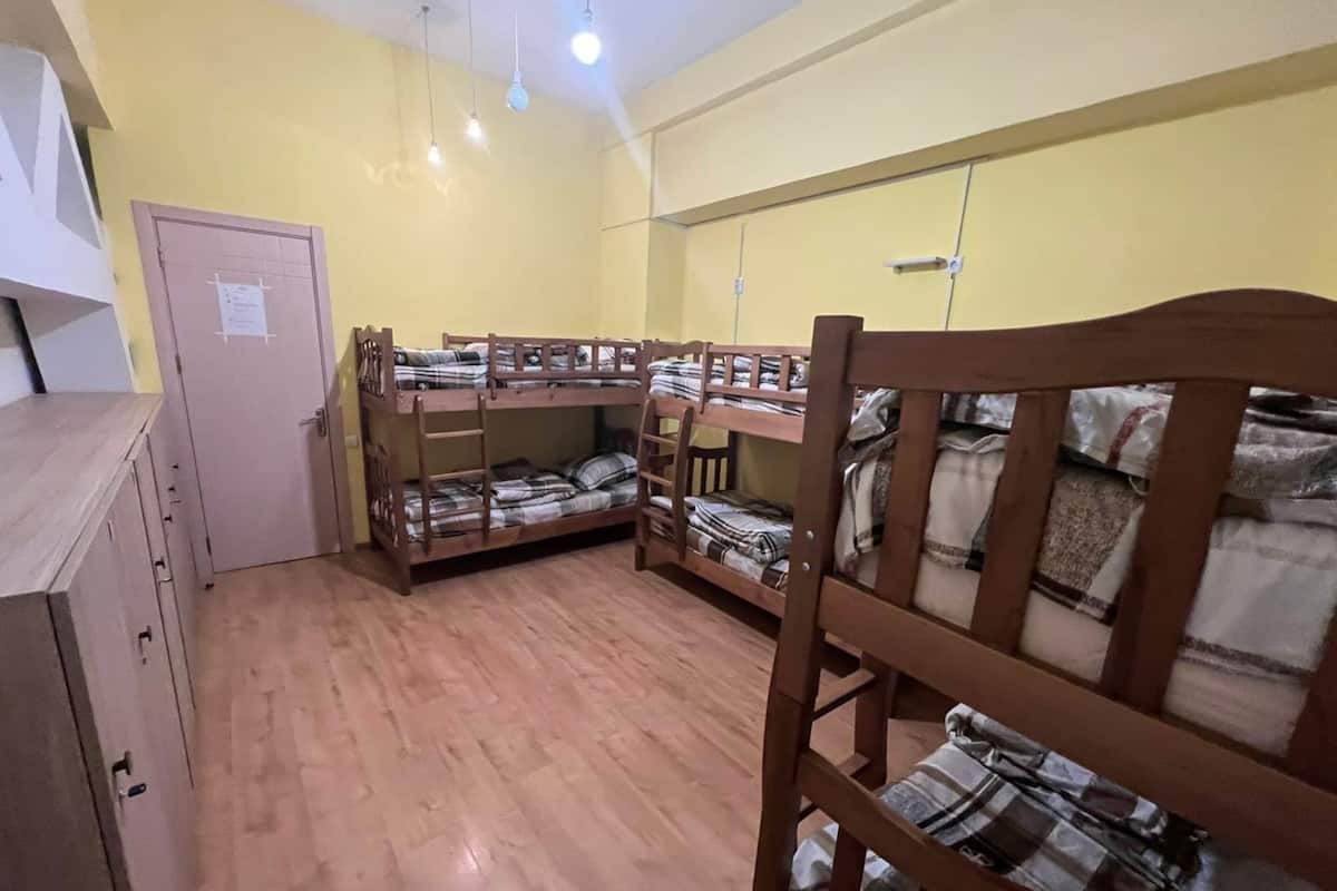 A dormitory room with bunk beds, wooden furniture, and a door with a notice.