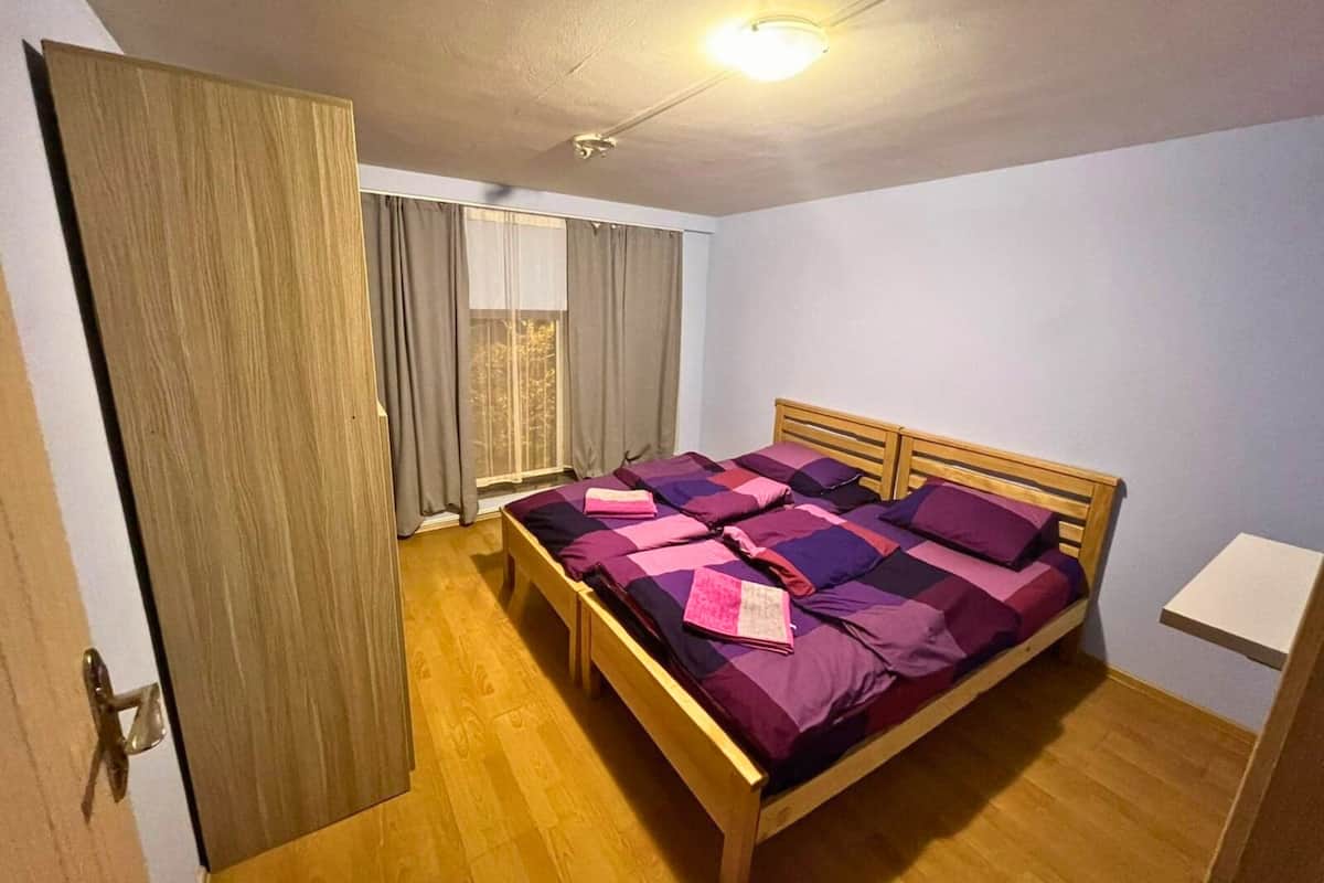 A bedroom with a wooden bed, a nightstand, a wardrobe, and a window with curtains.