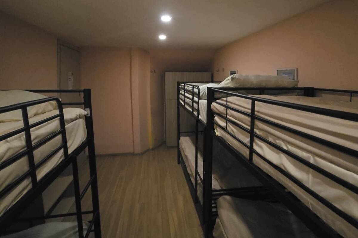 A dormitory room with bunk beds, a wooden floor, and a ceiling light.