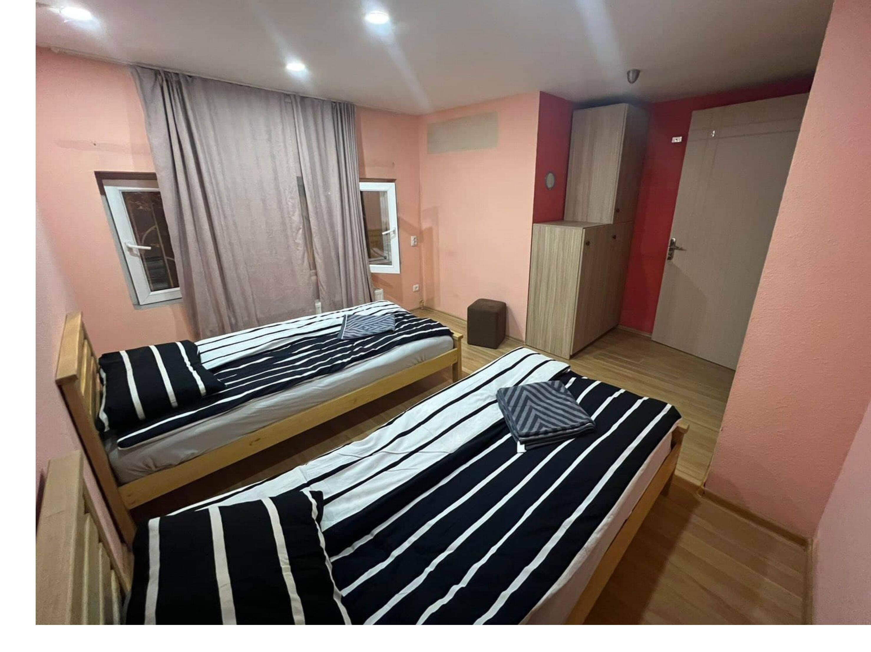 Une chambre avec deux lits, une armoire, un petit tabouret et une fenêtre avec des rideaux.