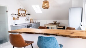 Une cuisine moderne dotée d’un grand îlot central en bois, de deux chaises, d’un luminaire suspendu et d’un réfrigérateur.