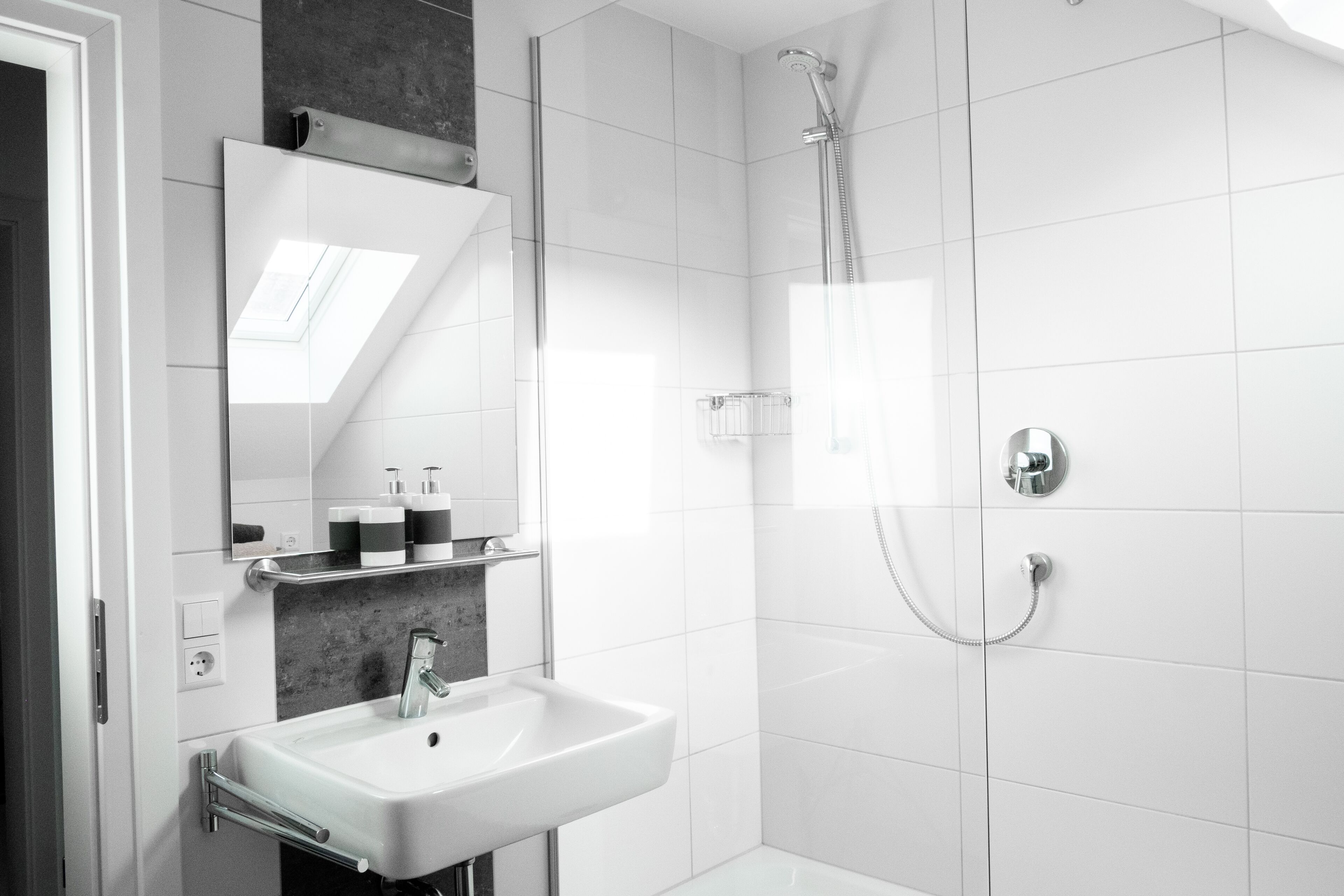 Une salle de bain moderne avec un lavabo blanc, un miroir, une douche et un porte-serviettes.