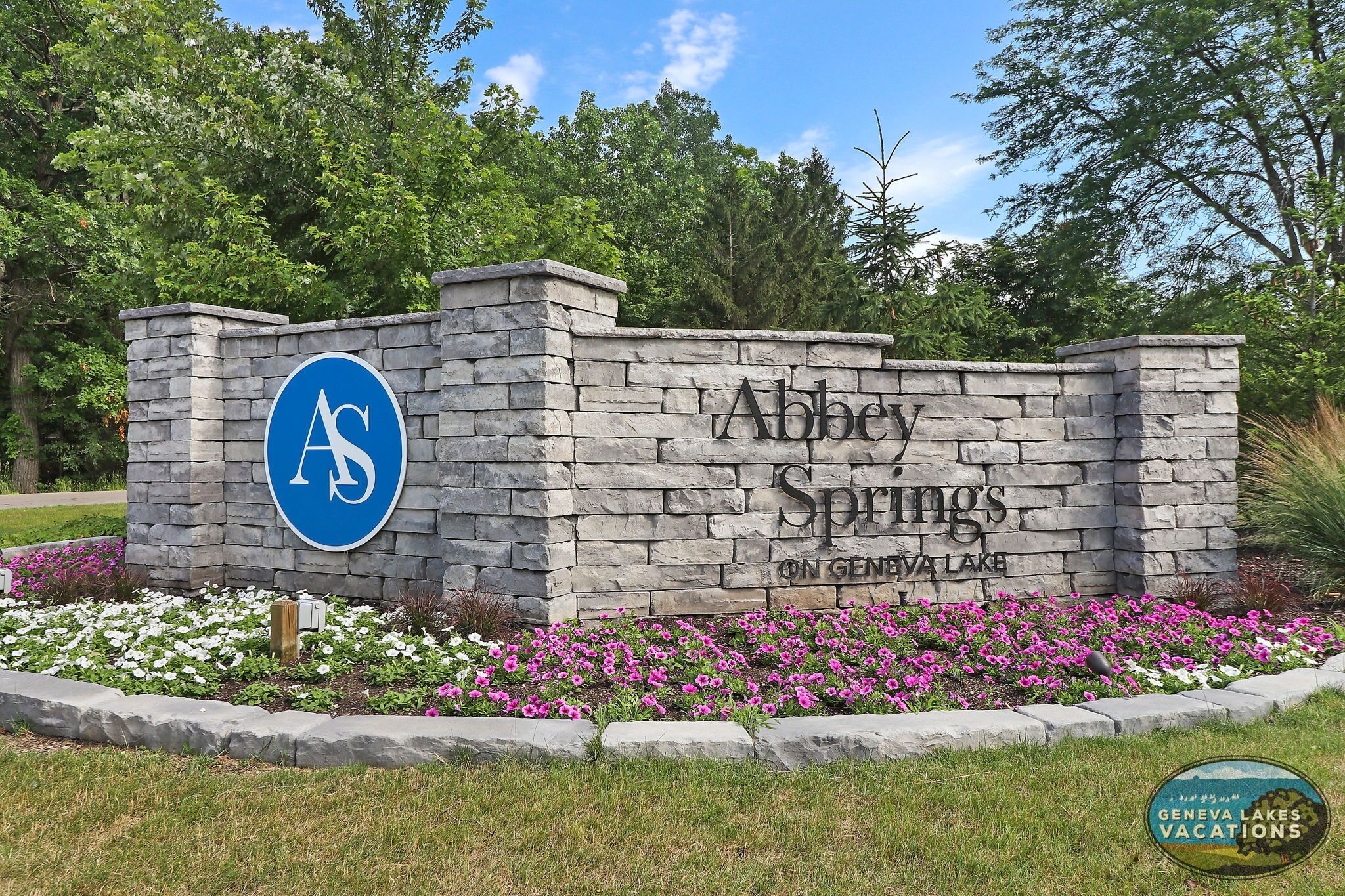 Eine Steinmauer mit dem Schriftzug "Abbey Springs on Geneva Lake" und einem blauen Logo, das einen weißen 'A' und 'S' zeigt.