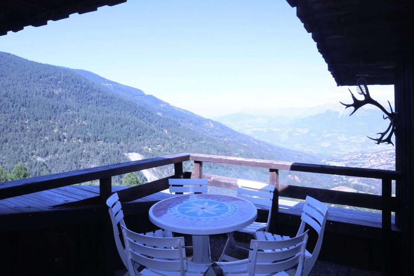 A wooden deck with a table and chairs, overlooking a mountainous landscape.