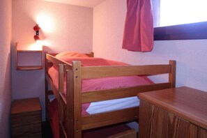 A bunk bed with a wooden frame, a small bedside table, and a wall-mounted shelf.