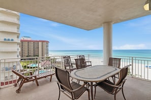 A balcony with a table and chairs, overlooking a beach and a hotel building.