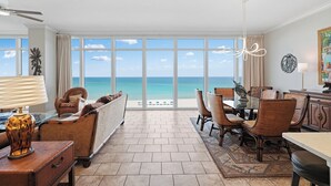 Una stanza spaziosa con un'ampia finestra vista sull'oceano, un'area pranzo con sedie in vimini e una ventola a soffitto.