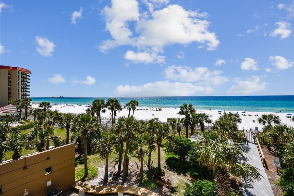Vista de la playa con palmeras, cielo despejado y un hotel al fondo.