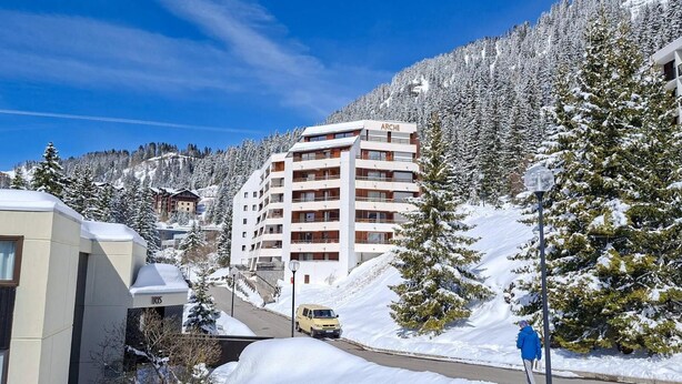 Een meerhoog hotel met balkons, omgeven door met sneeuw bedekte bomen en een heldere lucht.