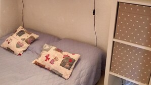 Een slaapkamer met een bed, twee bedlampen, een plank boven het bed en een opbergmeubel met lades.