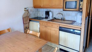 Een kleine keuken met houten kastjes, een magnetron, een spoelbak en een vaatwasser.