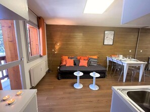 Une pièce de taille modeste comprenant un lit, une table à manger avec des chaises, un petit coin cuisine et une fenêtre avec des rideaux.