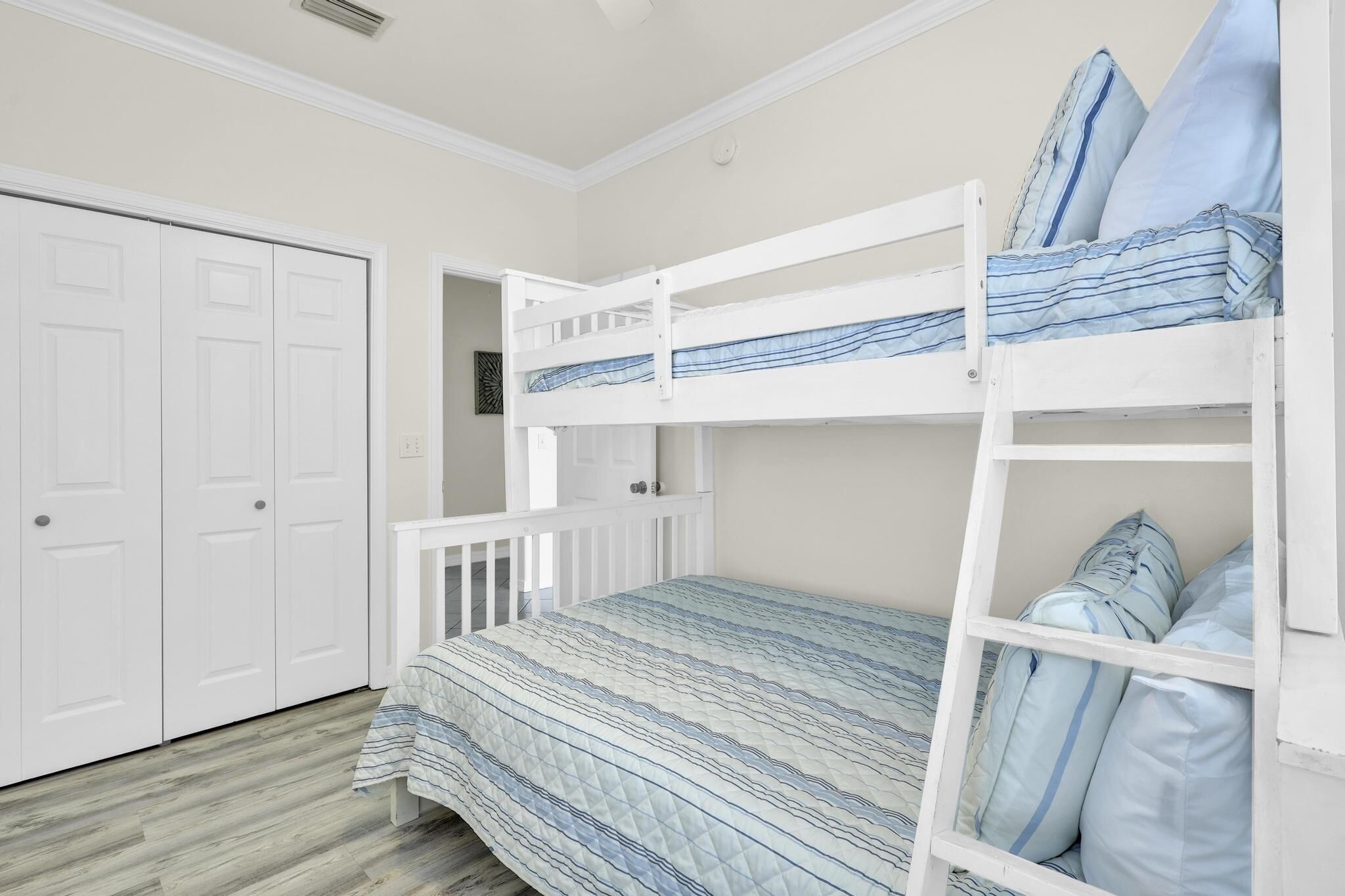 Un lit superposé avec une couvre-lit à rayures, une porte blanche et une armoire blanche.