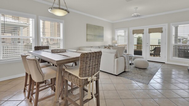 A spacious dining area with a wooden table and chairs, a wicker chair, and a hanging light fixture. - Spinnaker Pointe 3b 3 Bedroom Duplex by RedAwning (Gulf Shores)
