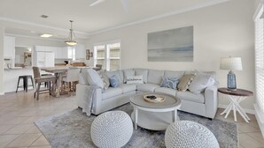 A spacious living room with a large L-shaped sectional sofa, a round coffee table, and a dining area with a wooden table and chairs. - Spinnaker Pointe 3b 3 Bedroom Duplex by RedAwning (Gulf Shores)