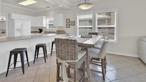 A modern kitchen with white cabinetry, a central island with stools, and a dining area with chairs. - Spinnaker Pointe 3b 3 Bedroom Duplex by RedAwning (Gulf Shores)