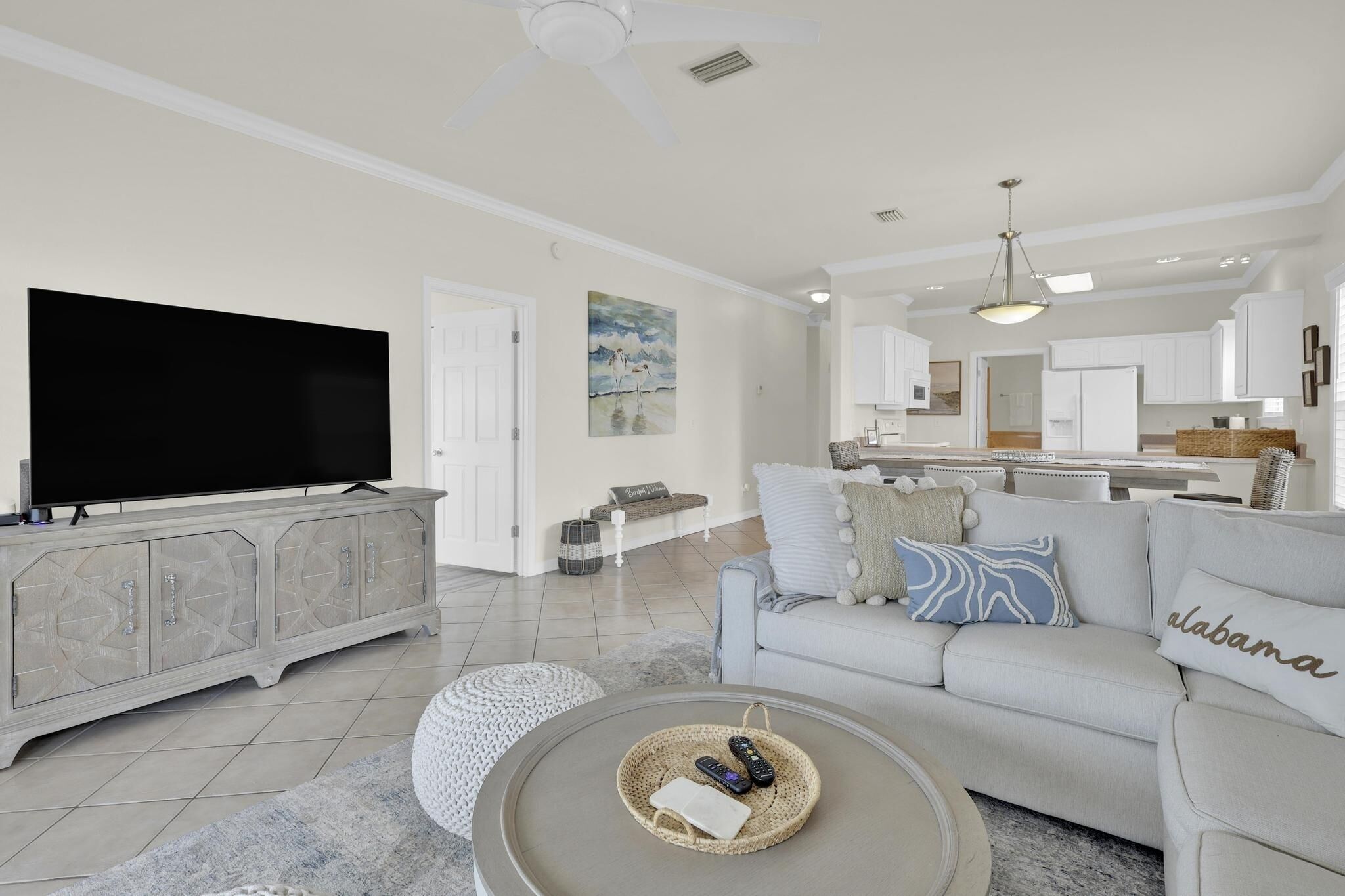 A modern living room with a flat-screen TV, grey sofa, and a coffee table with remote controls.