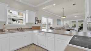 A spacious kitchen with white cabinetry, a large island, and a dining area visible through the windows. - Spinnaker Pointe 3b 3 Bedroom Duplex by RedAwning (Gulf Shores)