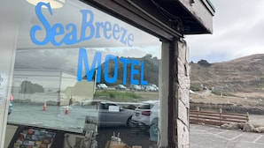 A motel with a large sign reading "SeaBreeze Motel" and a view of parked cars and a hill in the background. - Sea Breeze Motel (Pacifica)
