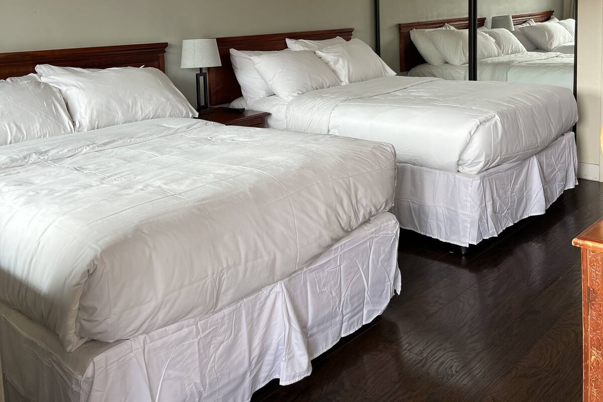 A hotel room with two beds, wooden headboards, white bedding, a nightstand, a lamp, and a large mirror.