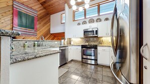 A modern kitchen with granite countertops, stainless steel appliances, and a herringbone wood ceiling.
