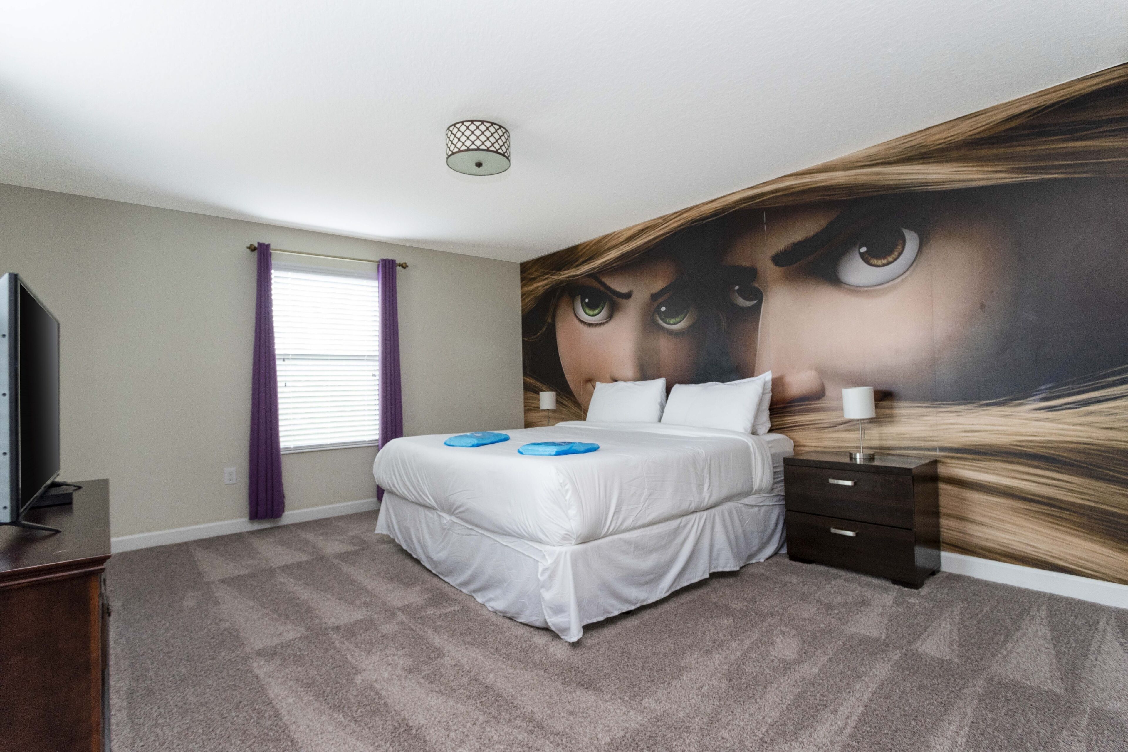 A bedroom with a large bed, a TV, a dresser, and a wall mural.