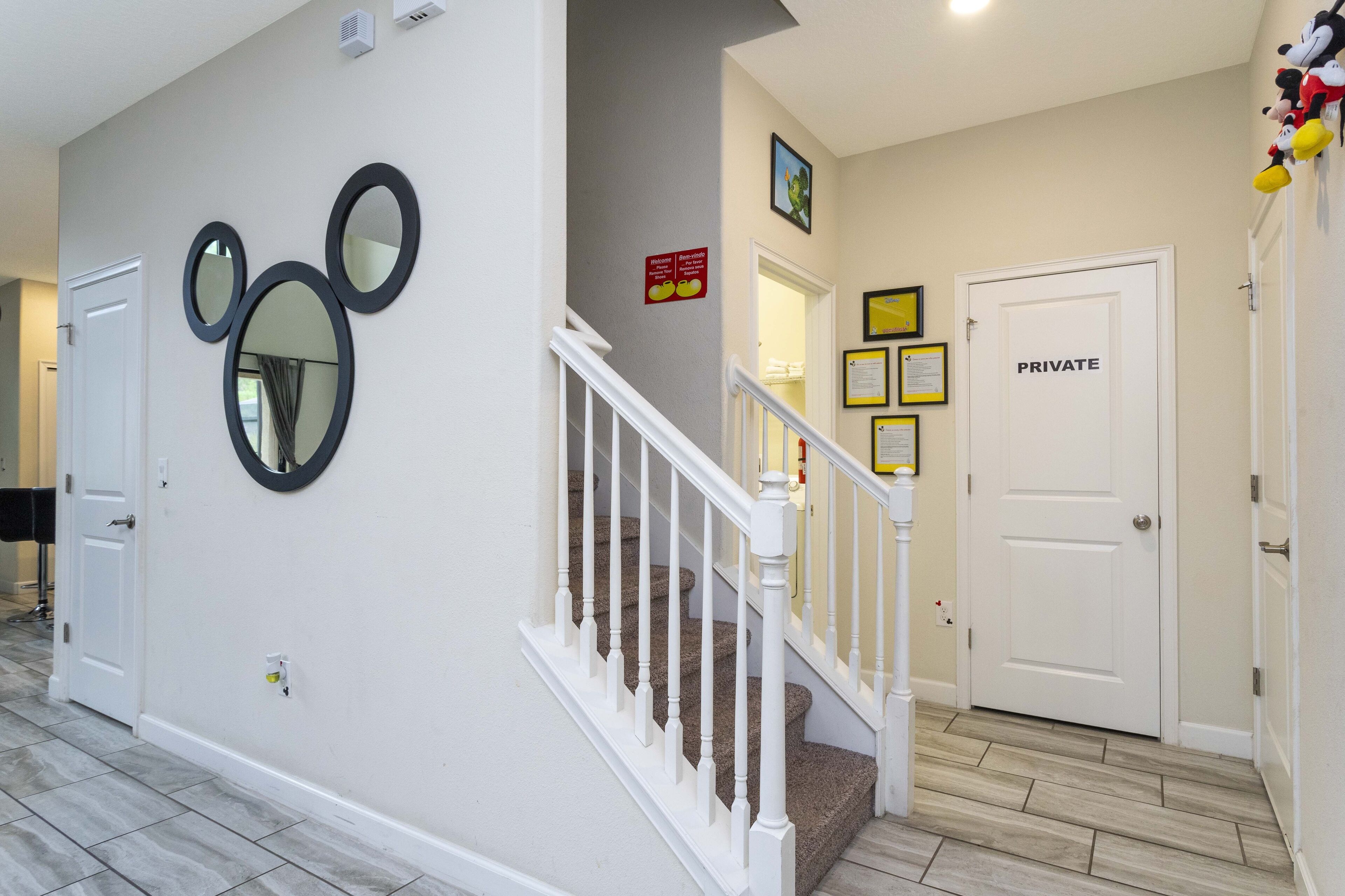 Ein Flur mit Treppe, einer Zimmertür und Wandspiegeln mit Mickey Mouse Motiv.