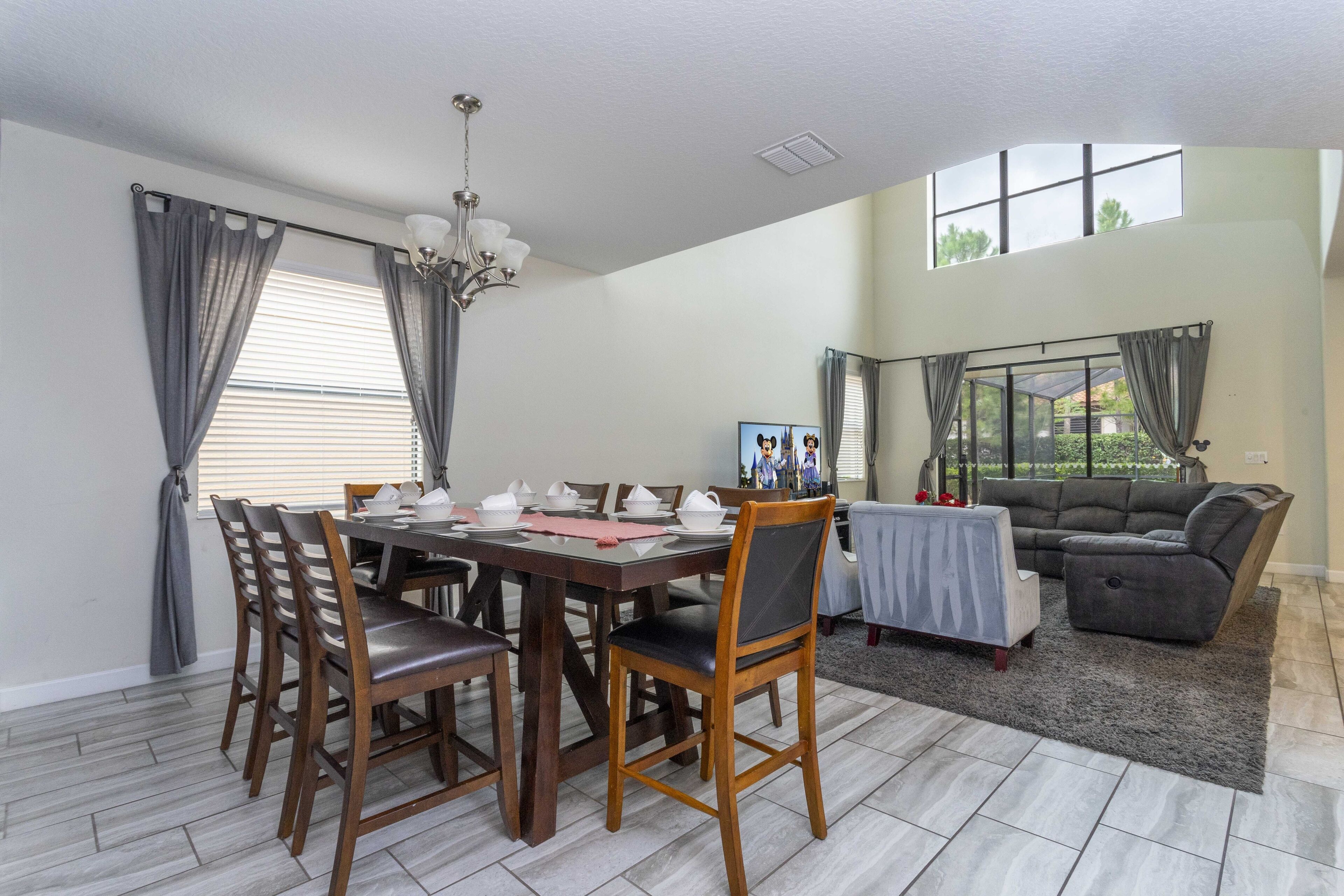 A dining area with a wooden table and chairs, a chandelier, and a sofa in the background.