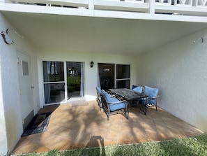 A patio with a table and chairs, a sliding glass door, and a white exterior wall.