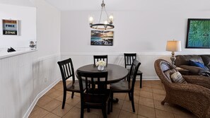 A dining area with a round table, chairs, a chandelier, a wall-mounted picture, and a couch with a lamp. - 114 El Matador 1 Bedroom Condo by RedAwning (Fort Walton Beach)