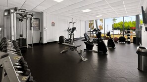 A gym with various exercise equipment, a wall-mounted weight rack, and a window providing a view of the outdoors.