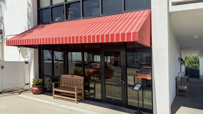A building with a red awning, a bench, and a potted plant outside. - 114 El Matador 1 Bedroom Condo by RedAwning (Fort Walton Beach)