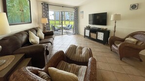 Ein Wohnzimmer mit einer Couch, Sesseln, einem Fernseher und Blick ins Freie.
