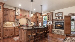 A spacious kitchen with wooden cabinets, a stone fireplace, and a bar area with stools. - Base Camp At Iron Horse... 4 Bedroom Townhouse by RedAwning (Winter Park)