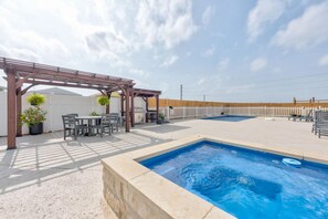 Ein Poolbereich mit Pergola, Sitzgelegenheiten und Grill.