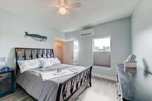 Ein Schlafzimmer mit Bett, Nachttisch, Kommode, Deckenventilator und Fenster.