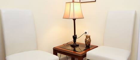 Une pièce avec deux chaises blanches, une petite table en bois avec une lampe et un vase.