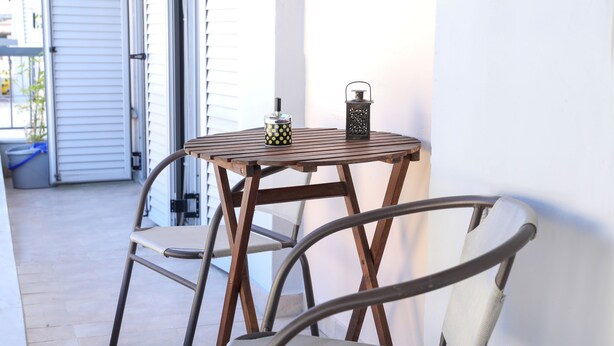 Une table en bois, deux chaises, une lanterne et un récipient sur un balcon.
