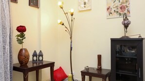 Un salon doté d’un plancher en bois, d’un vase rouge orné d’une fleur, de deux petites tables, d’un grand lampadaire et d’un meuble avec des portes en verre.