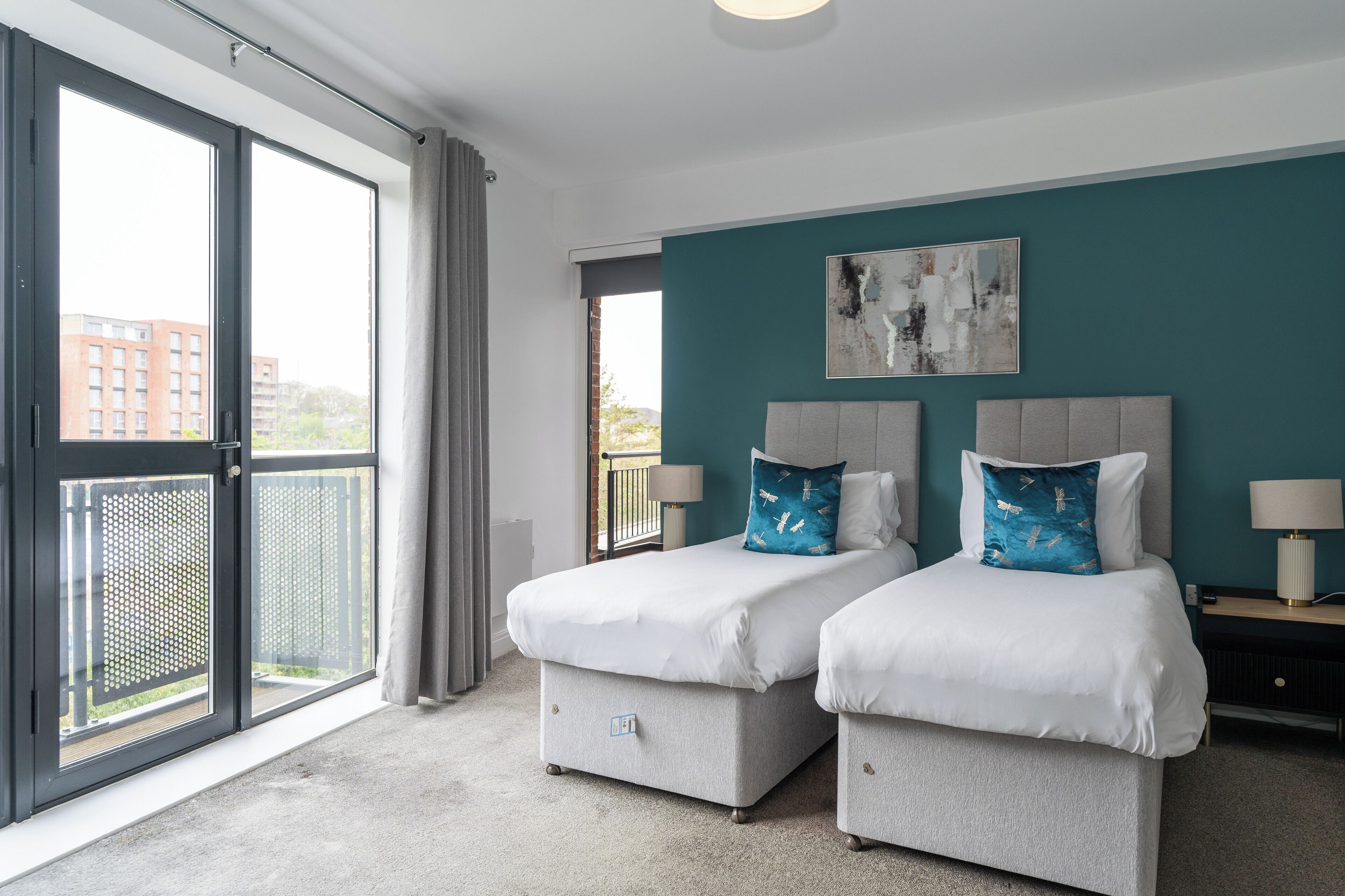 A hotel room with two beds, a balcony, and a view of buildings.