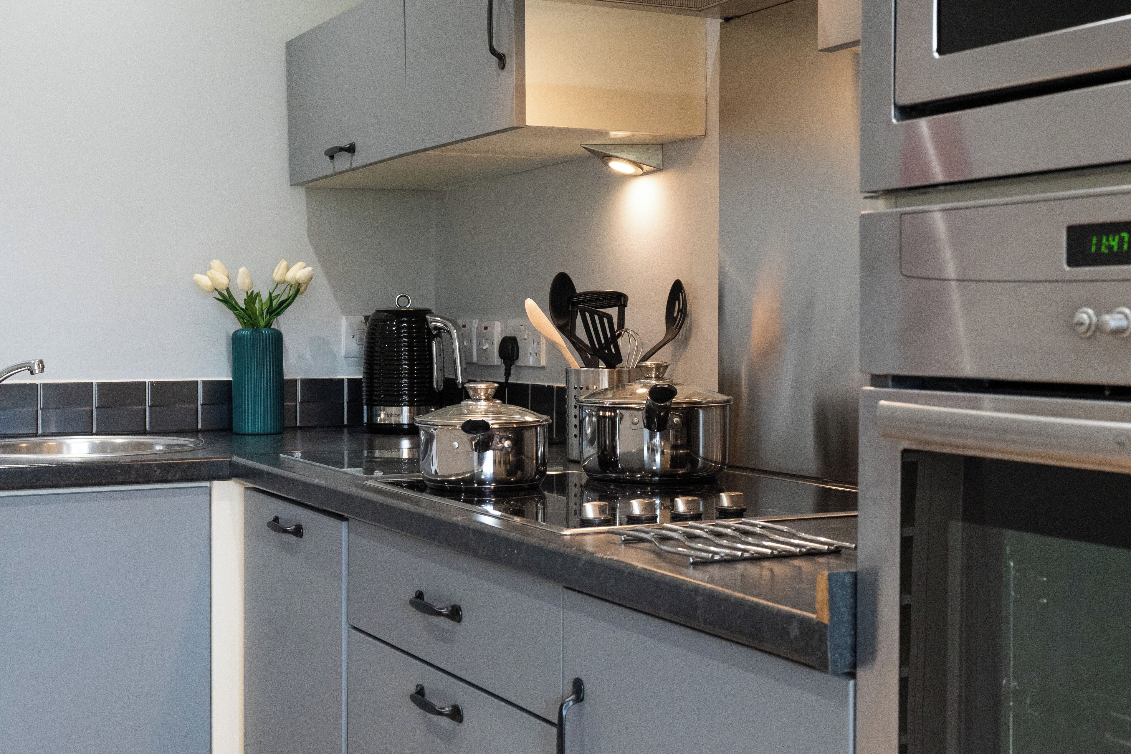 A modern kitchen with stainless steel appliances, a black countertop, and a teal vase with white flowers.