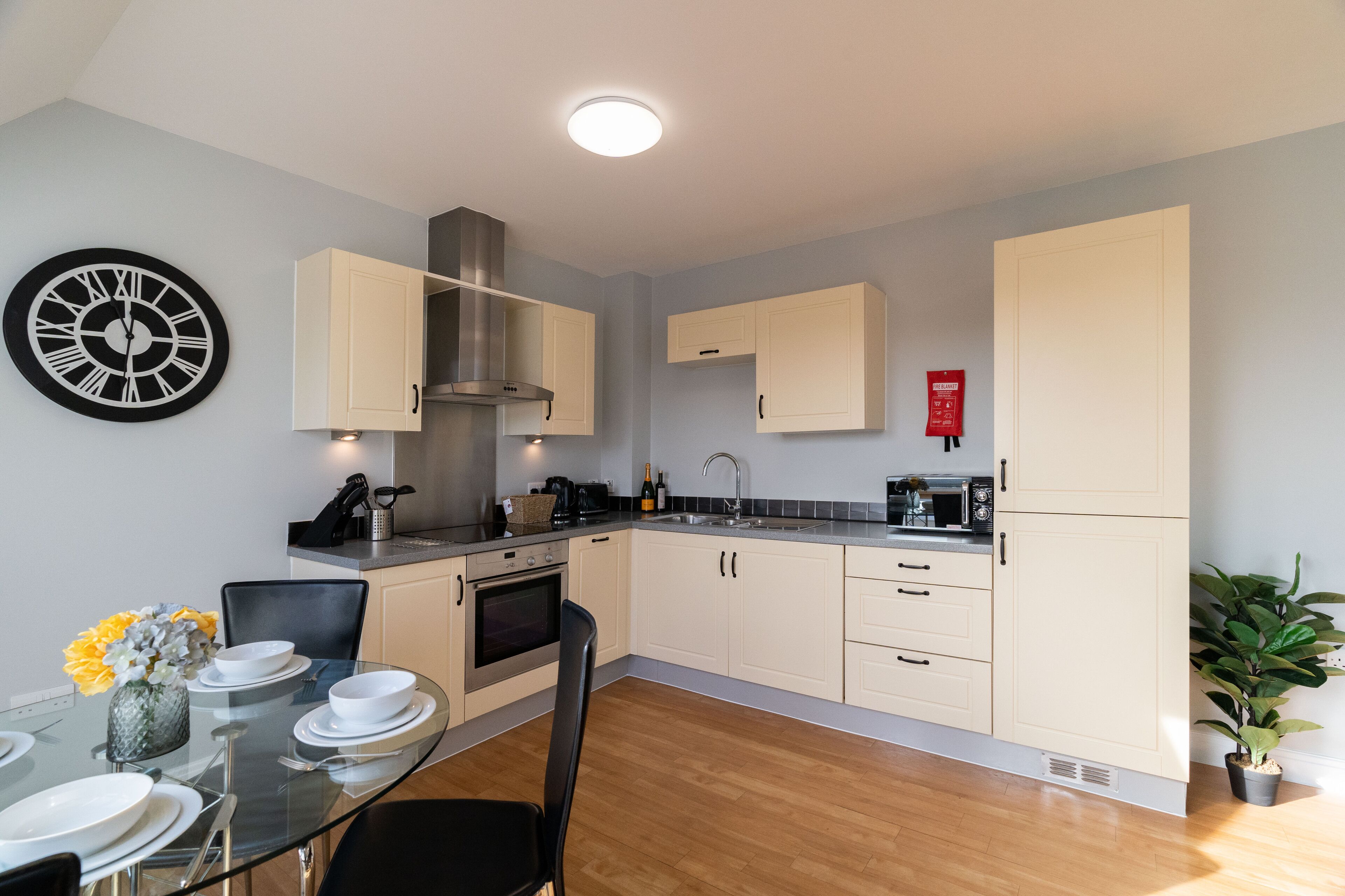 Una cocina moderna con armarios de color claro, una campana extractora de acero inoxidable y un comedor con mesa y sillas de vidrio.