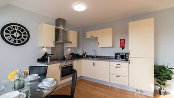 Una cocina moderna con armarios de color claro, una campana extractora de acero inoxidable y un comedor con mesa y sillas de vidrio.