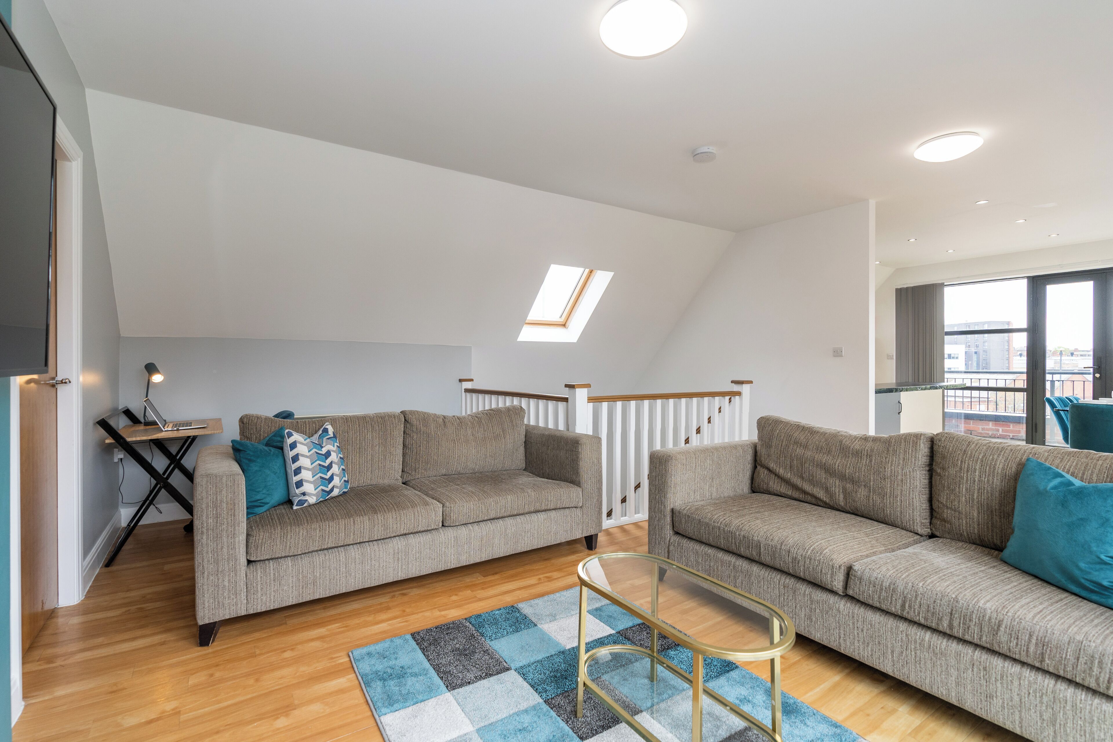 A spacious living room with two sofas, a glass coffee table, and a view of the city through large windows.